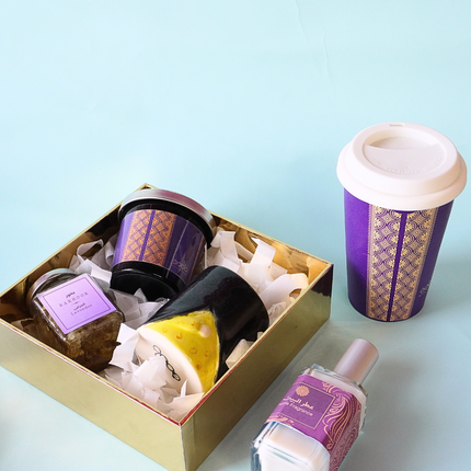 A candle , and mug inside gift box and one tumbler and home fragrance in the table